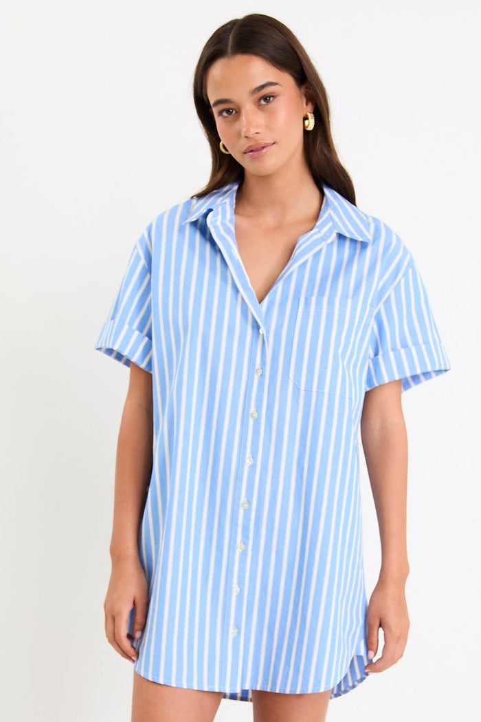 Model wearing a blue and white striped short sleeve mini shirt dress with a button front and collar.