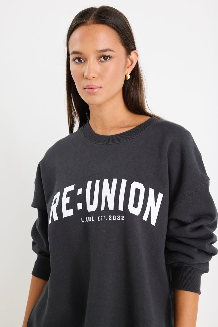 Woman wearing a charcoal grey oversized sweatshirt with "RE:UNION" printed across the chest, styled with light blue denim shorts.