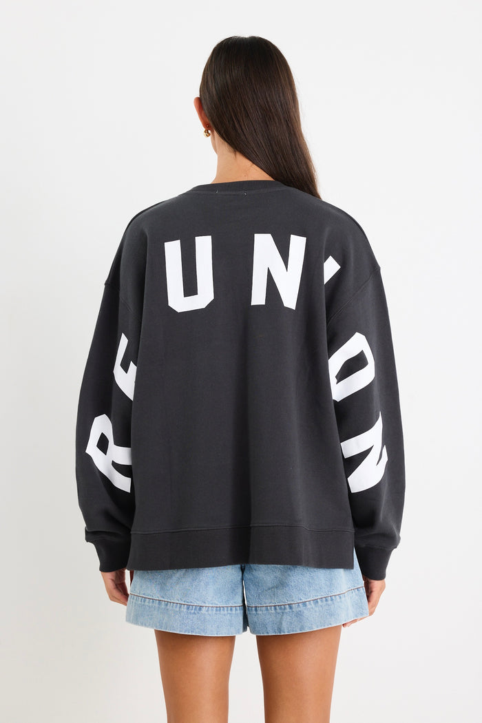 Woman wearing a charcoal grey oversized sweatshirt with "RE:UNION" printed across the chest, styled with light blue denim shorts.
@col_pattern