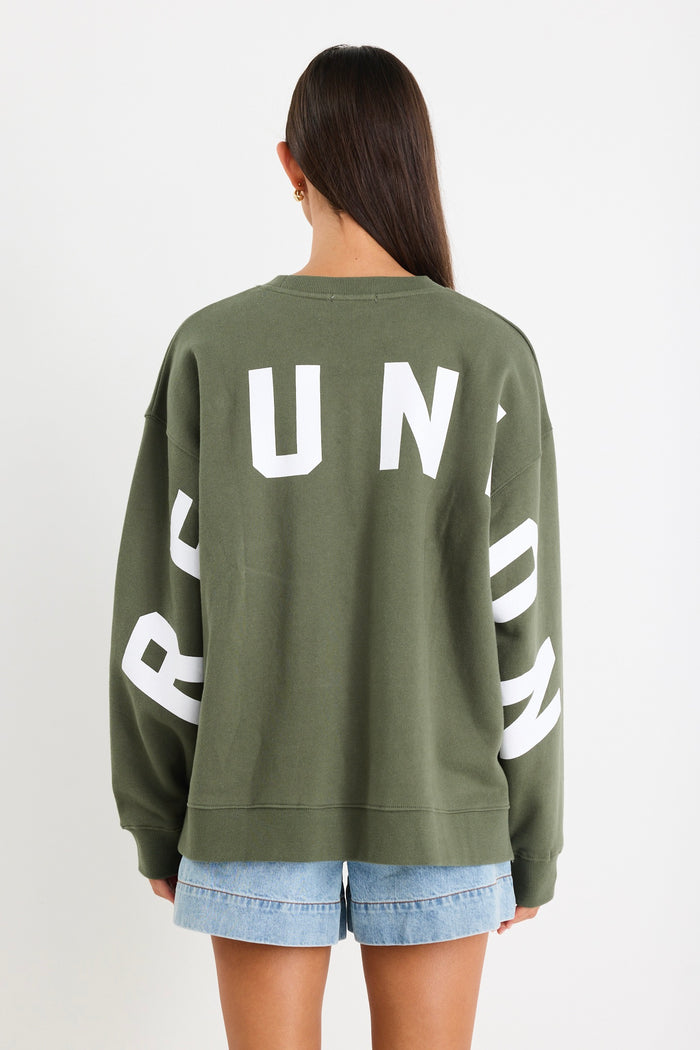 Woman wearing a khaki green oversized sweatshirt with "RE:UNION" printed across the chest, styled with light blue denim shorts.
@col_pattern
