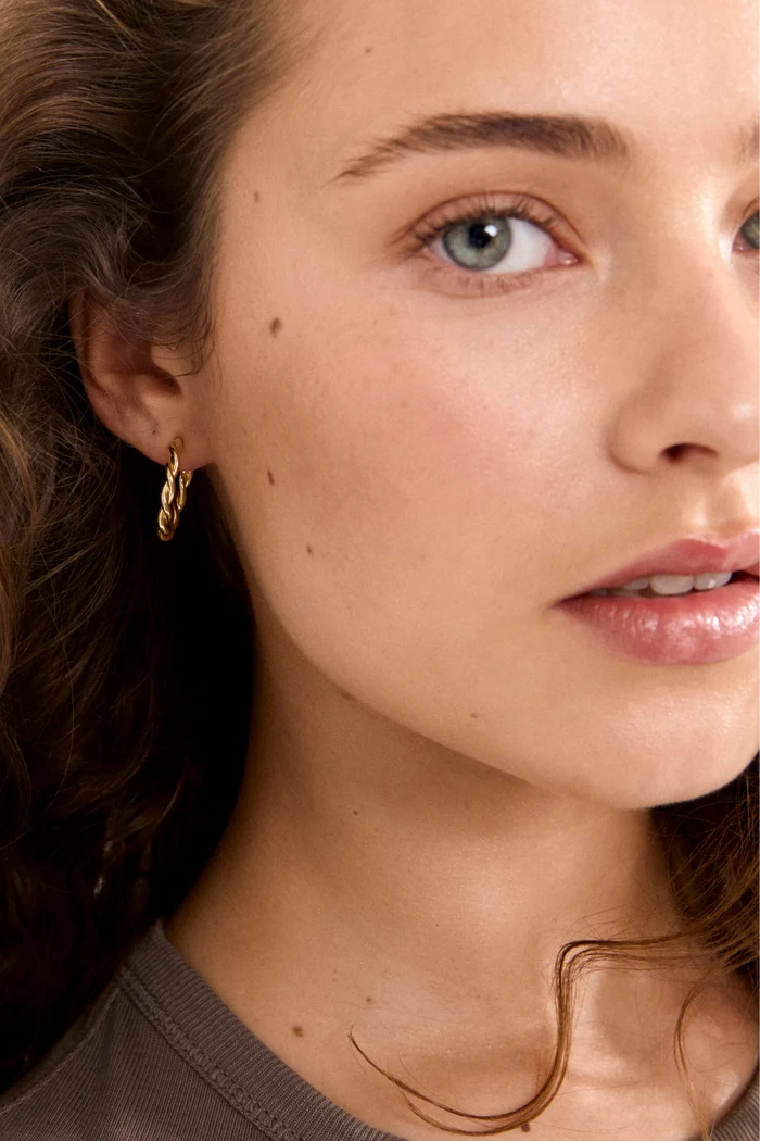 Close-up of a woman wearing gold hoop earrings with a neutral background