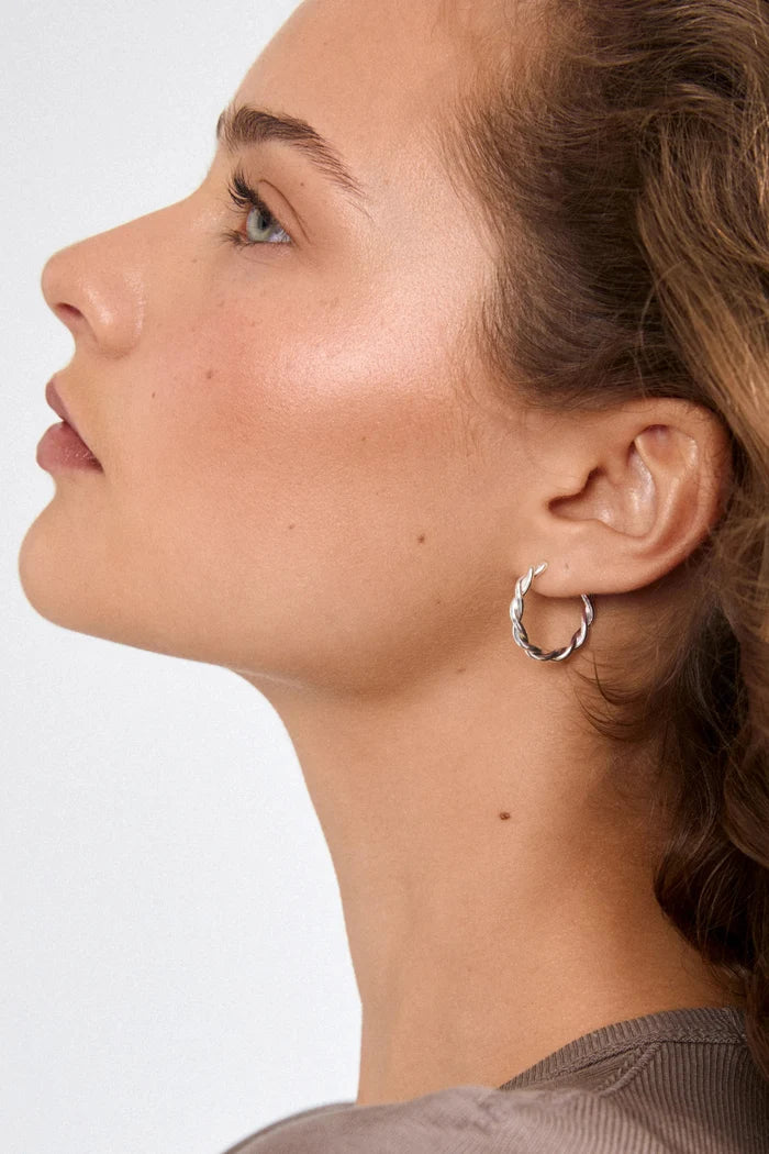Close-up of a woman wearing a silver hoop earring against a neutral background