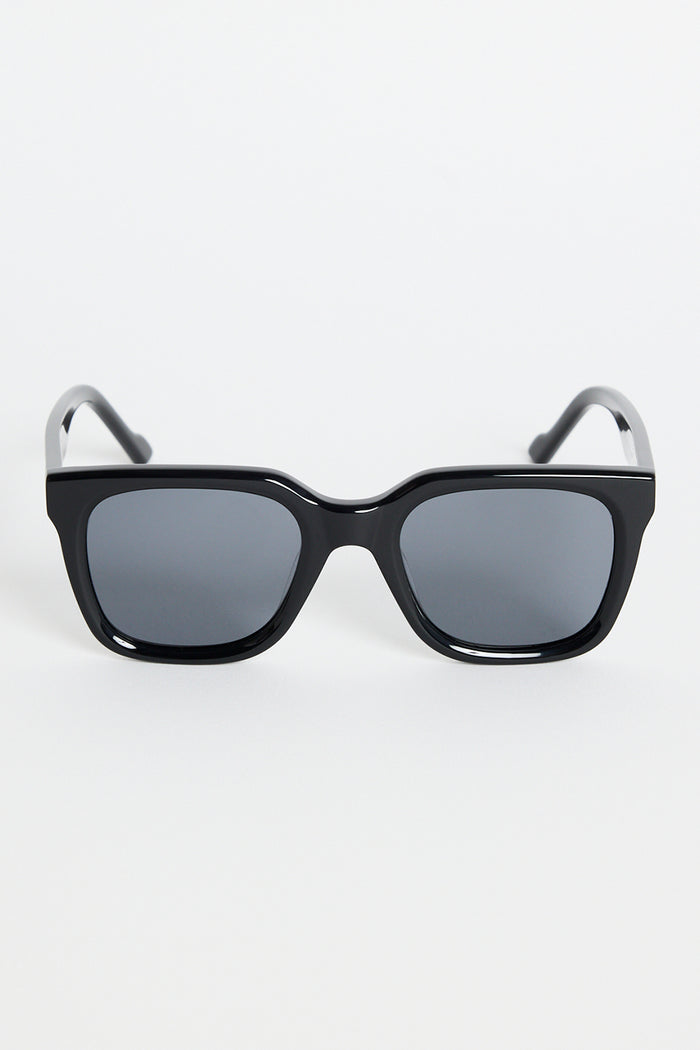 Glossy black rounded-square sunglasses with dark tinted lenses and RE:UNION label branding on the arm, photographed on a white background