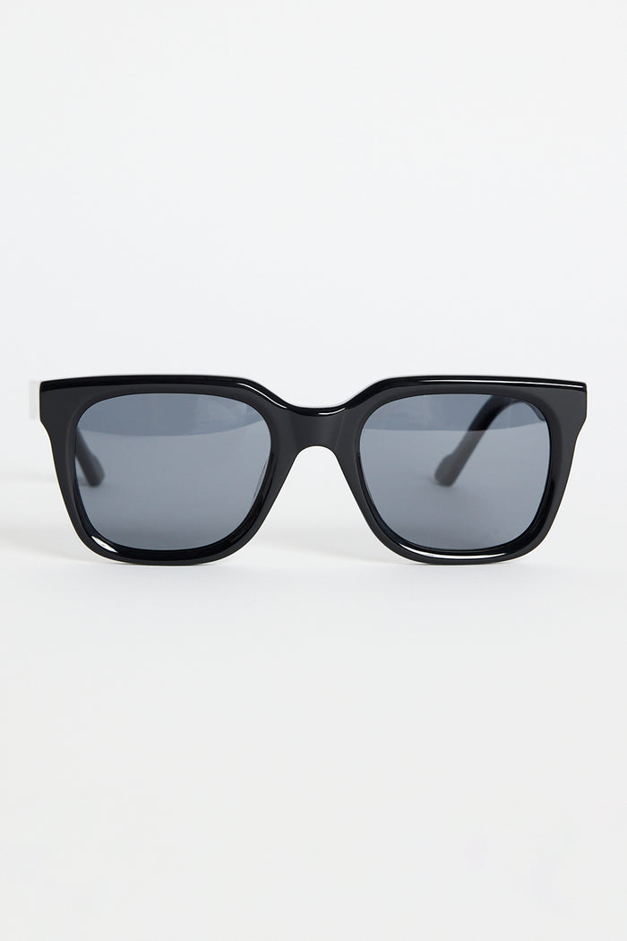 Glossy black rounded-square sunglasses with dark tinted lenses and RE:UNION label branding on the arm, photographed on a white background
