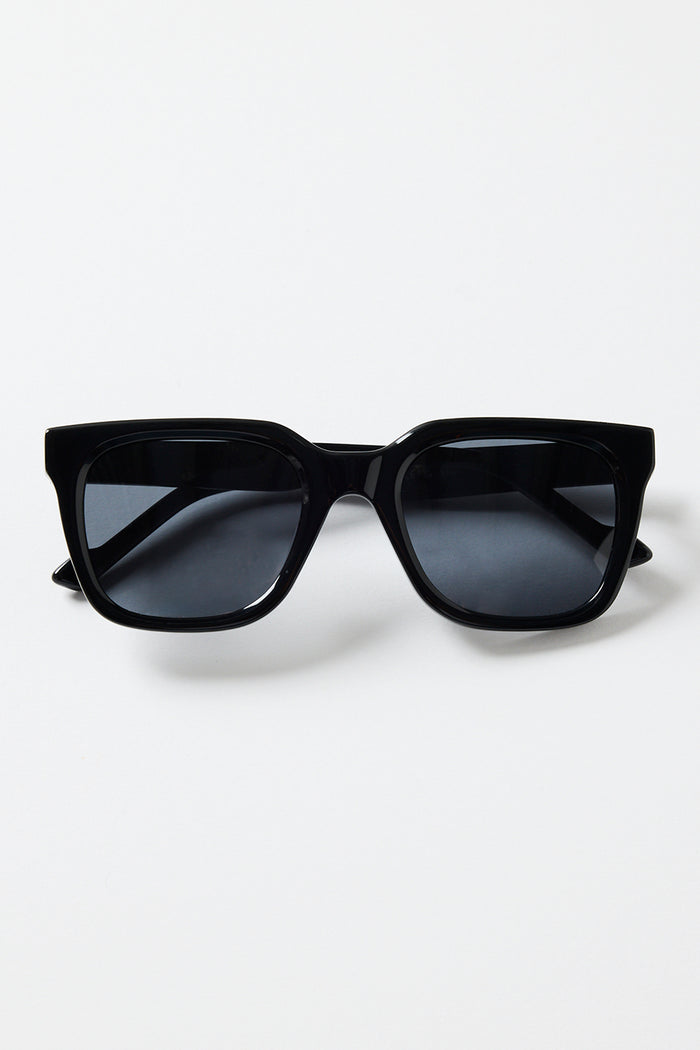 Glossy black rounded-square sunglasses with dark tinted lenses and RE:UNION label branding on the arm, photographed on a white background