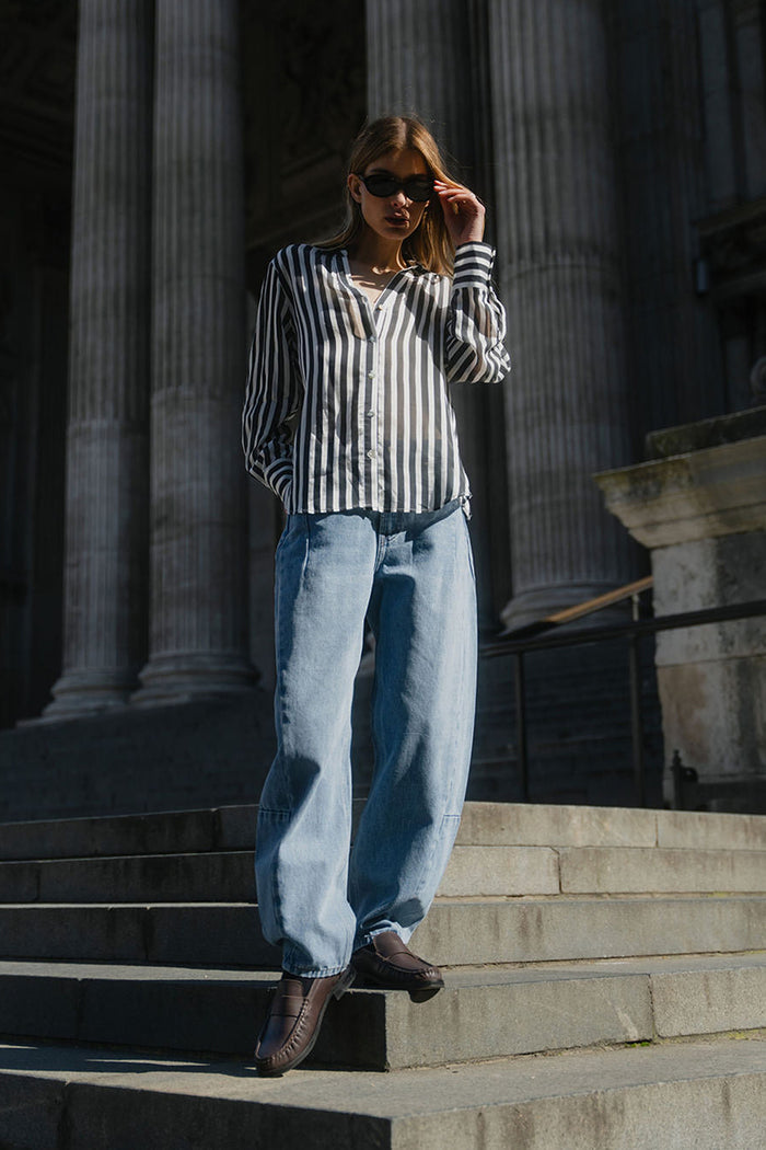 Person wearing a striped shirt and jeans standing on steps in front of classical architecture.