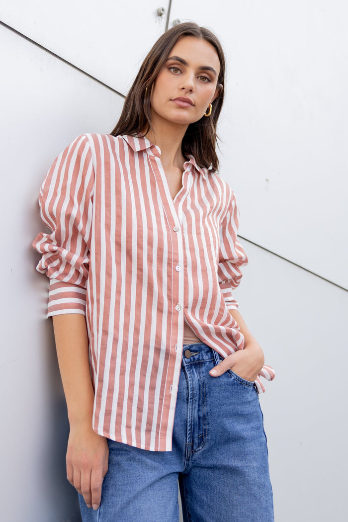 Woman wearing a red and white striped shirt and blue jeans against a white wall.