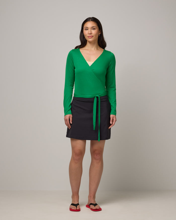 Model wearing Natalia Wrap Top in Verde, a bright Kelly green color. Natalia Wrap Top is a merino wool long sleeve, v-neck, slim fit top available in sizes XS-3X.