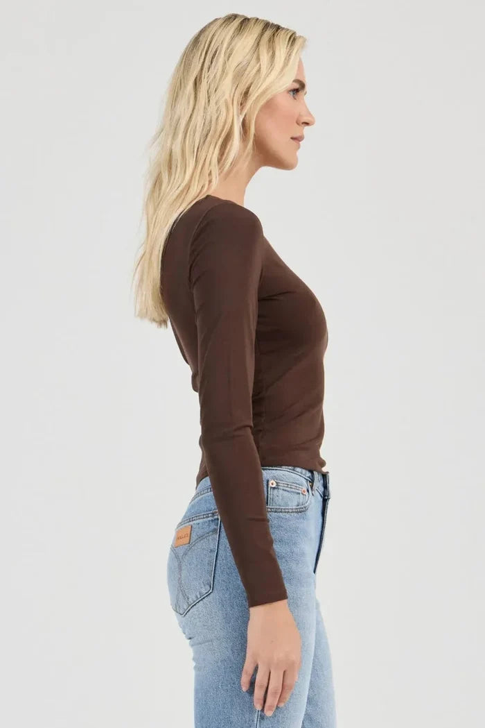 Woman wearing a brown long-sleeve top and light blue jeans on a white background