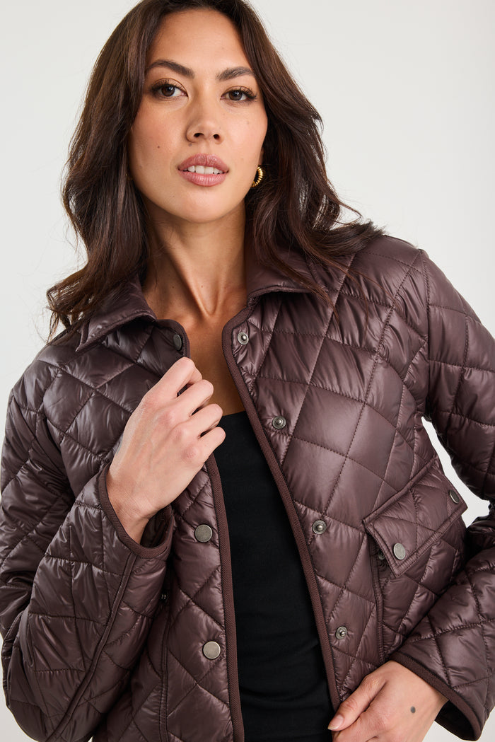 Woman wearing a quilted brown jacket against a white background