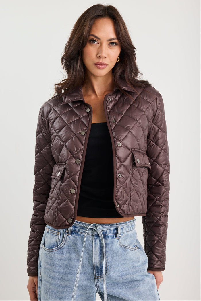 Woman wearing a quilted jacket, black top, and blue jeans on a white background