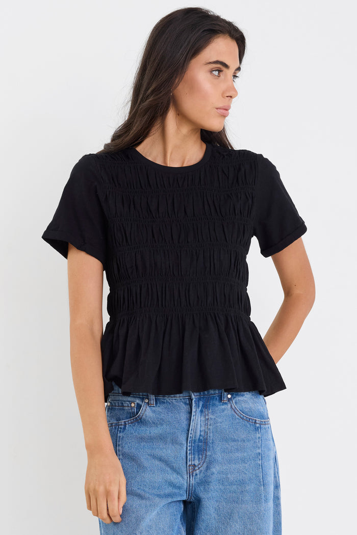 Woman wearing a black ruffled top and blue jeans against a white background