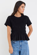 Woman wearing a black ruffled top and blue jeans against a white background