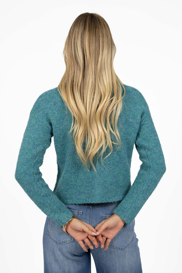 Person wearing a teal sweater and blue jeans on a white background