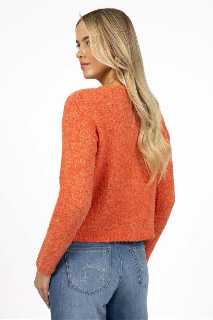 Woman wearing an orange sweater and blue jeans on a white background