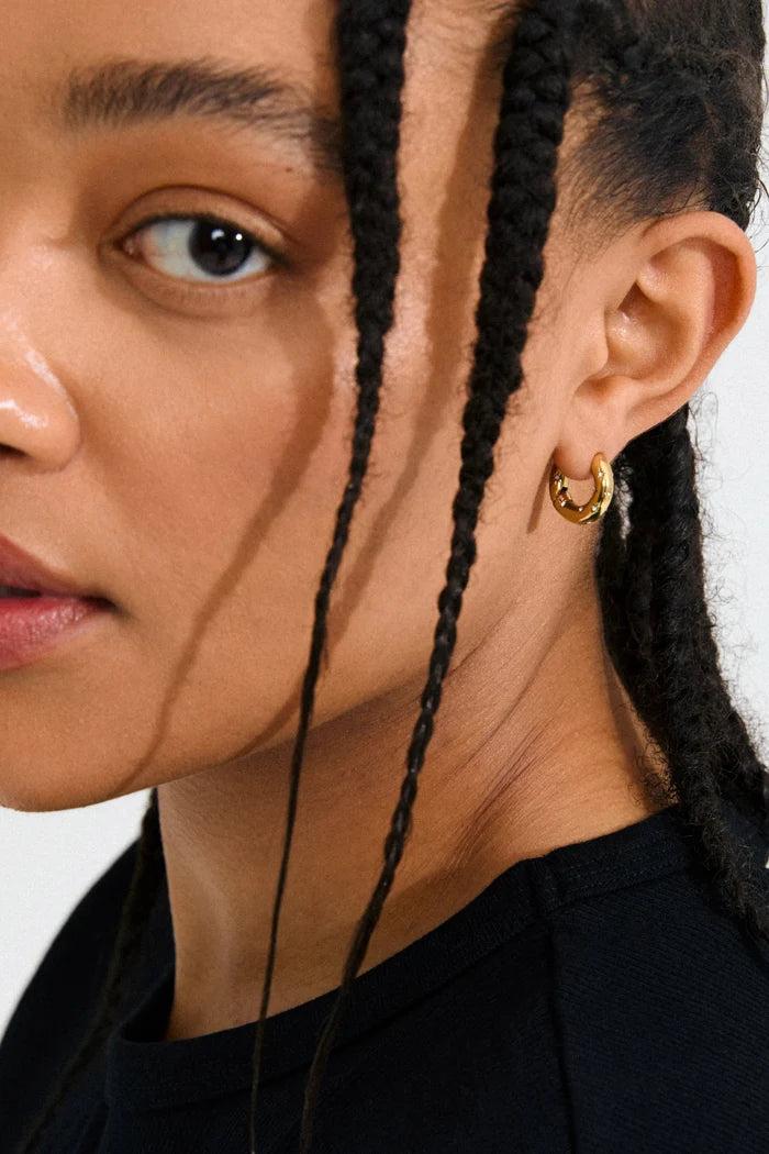 Close-up of a person wearing a gold hoop earring with a plain background