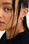 Close-up of a person wearing a gold hoop earring with a plain background