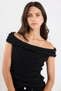 Woman wearing a black off-shoulder top against a white background