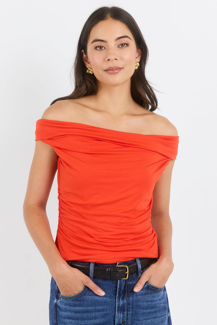 Woman wearing a red off-shoulder top and blue jeans on a white background