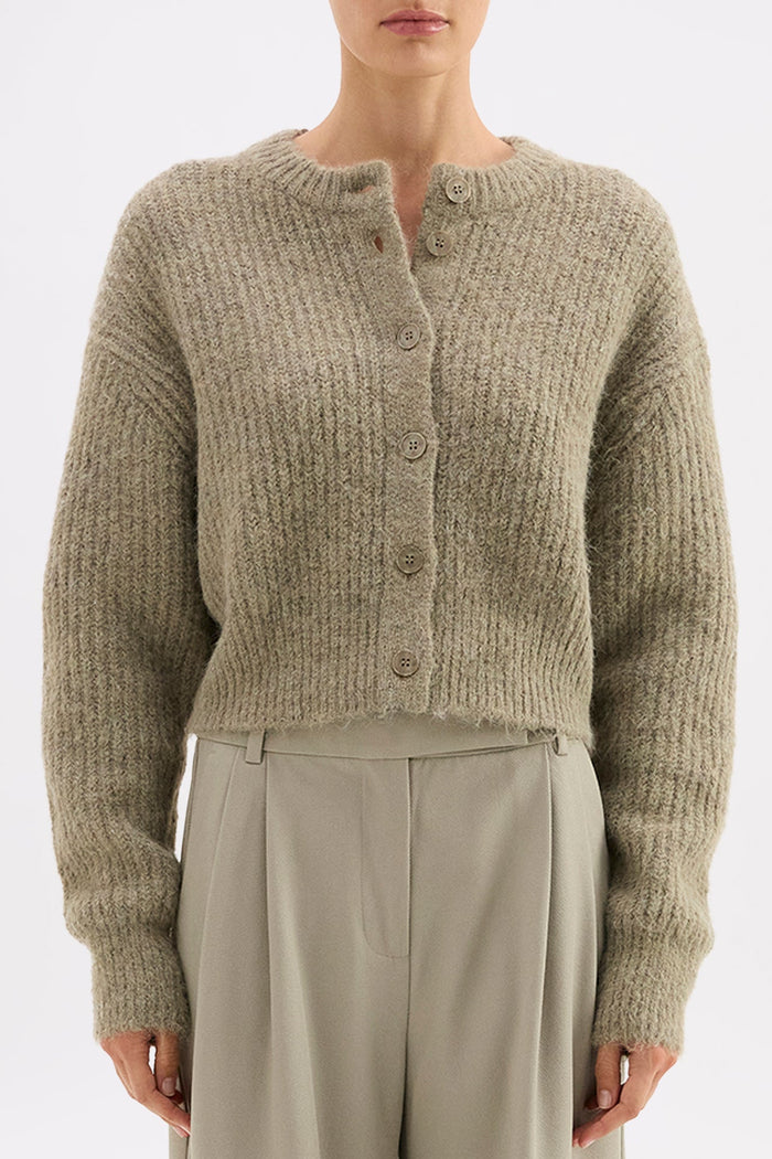 Person wearing a beige knitted cardigan and beige pants on a white background