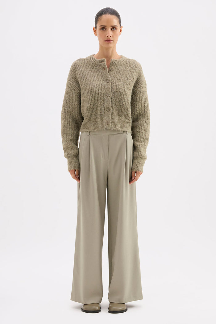 Woman wearing a patterned cardigan and beige pants on a white background
