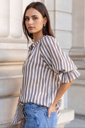 Woman in a striped shirt and jeans standing against classical architecture.
