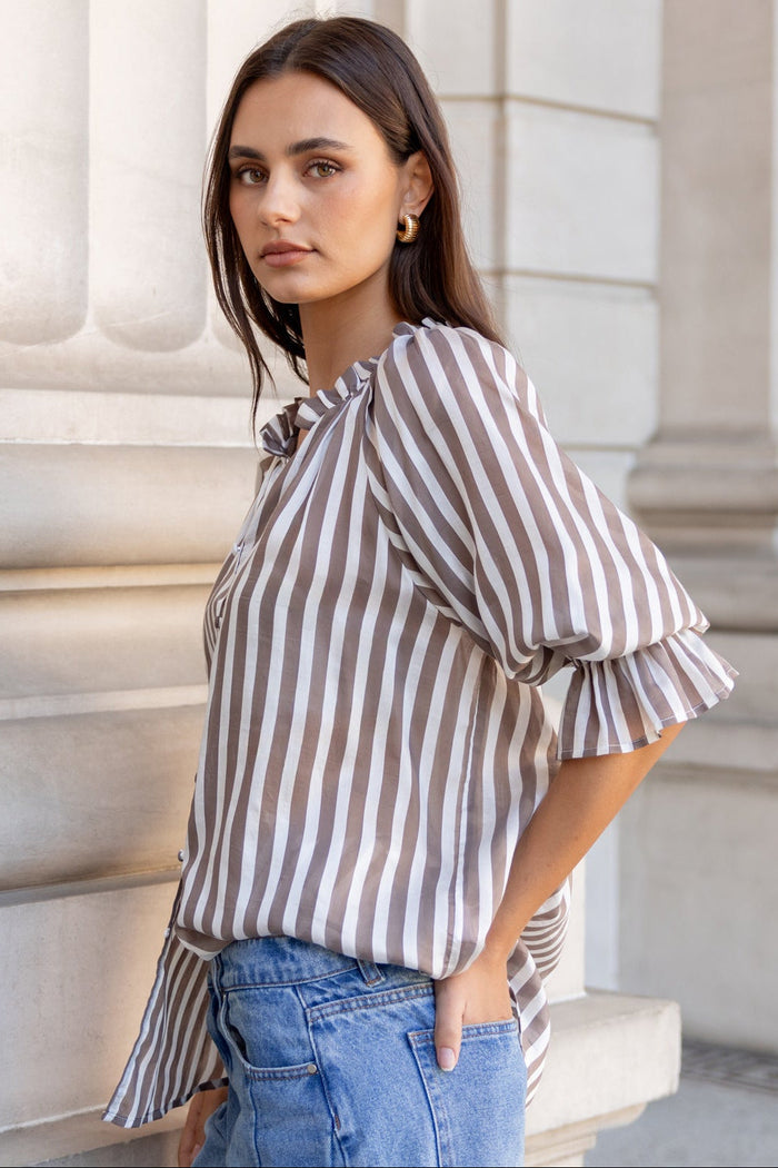 Woman in a striped shirt and jeans standing against classical architecture.