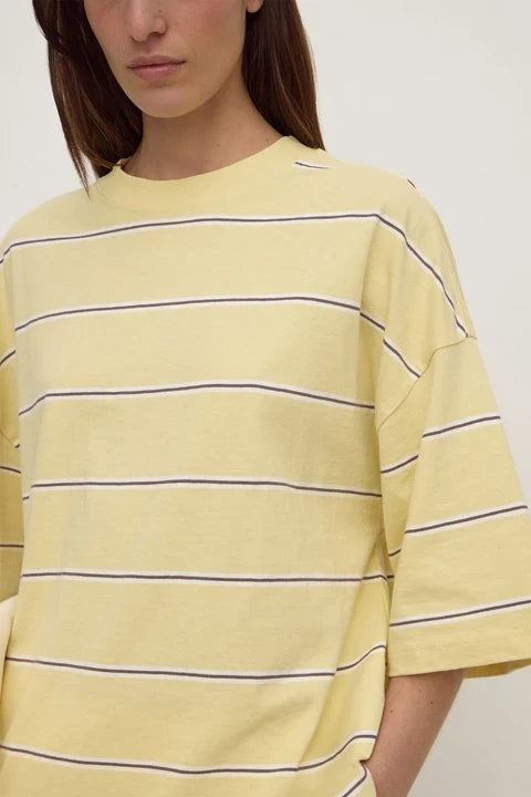A close-up of a model wearing an oversized pale yellow t-shirt with thin horizontal navy stripes.