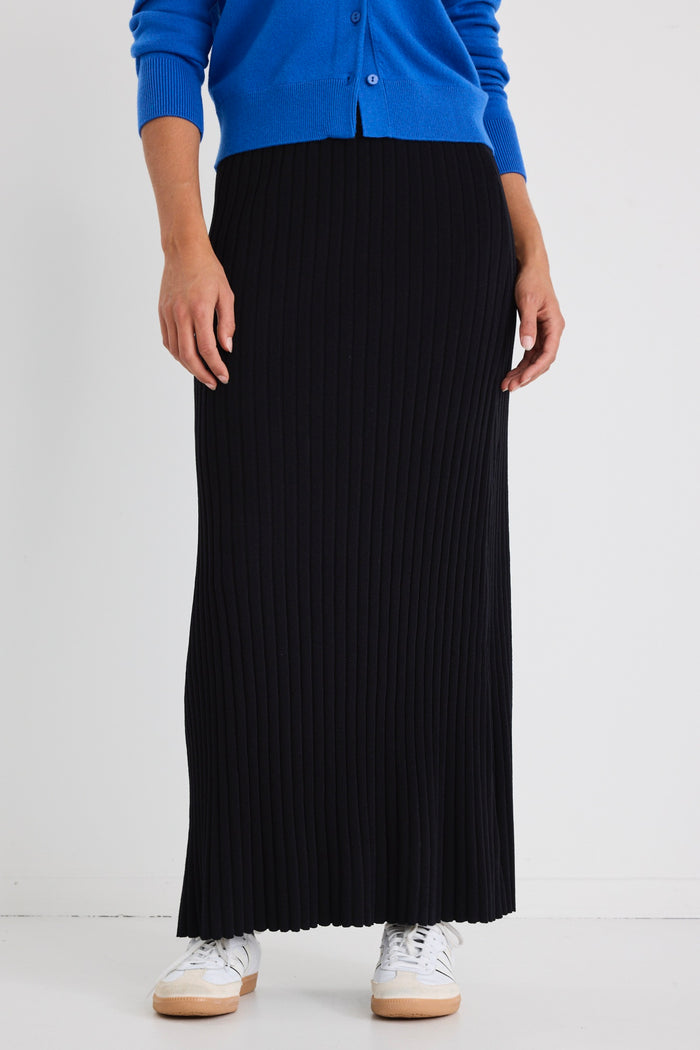 Woman wearing a white boxy tee tucked into a full-length black rib knit skirt with flared hem, styled with white sneakers.