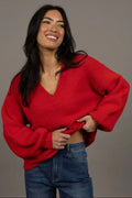 Woman wearing a red sweater and blue jeans against a gray background