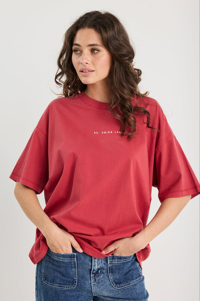 Woman wearing a red t-shirt and blue jeans against a plain background
