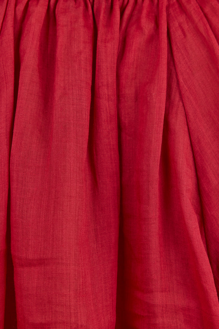 A close-up of a deep red or burgundy pleated fabric, showing the texture and folds of the material.