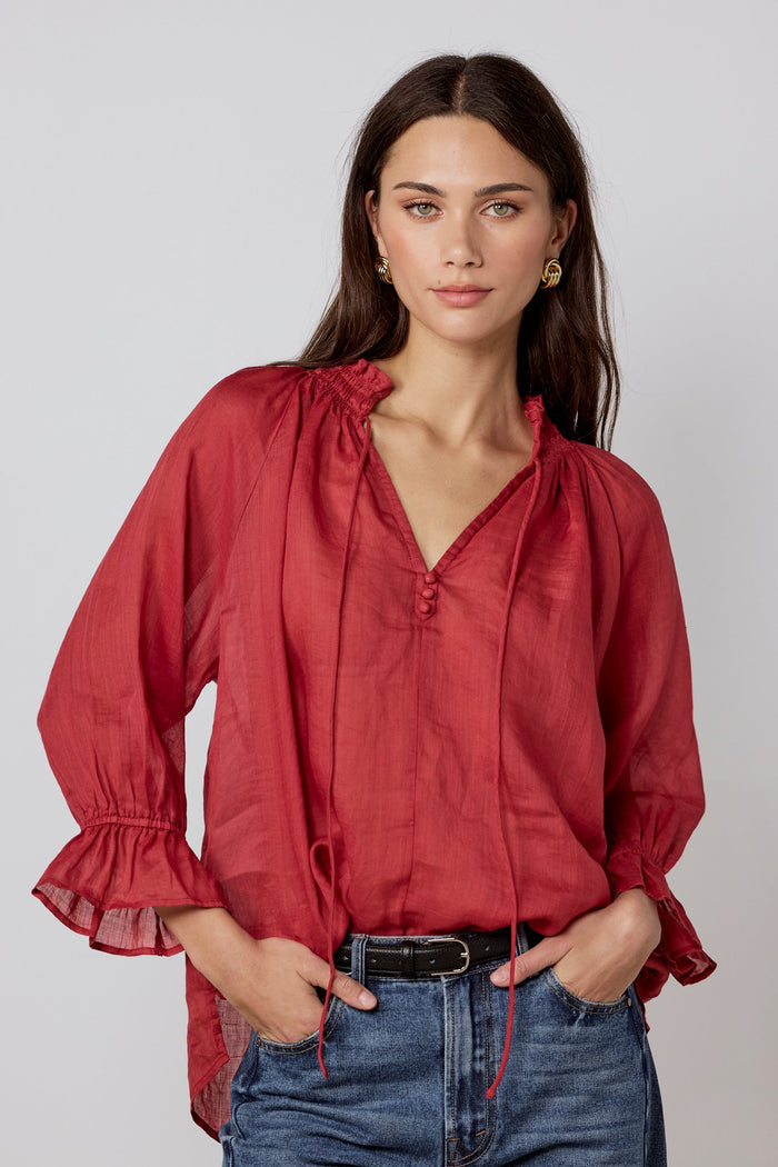 Woman wearing a red blouse and blue jeans against a plain background