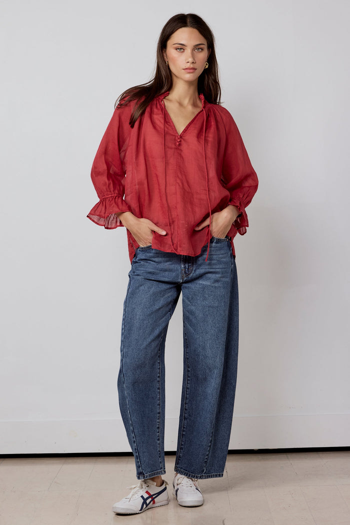 Woman wearing a red blouse and blue jeans against a white background
