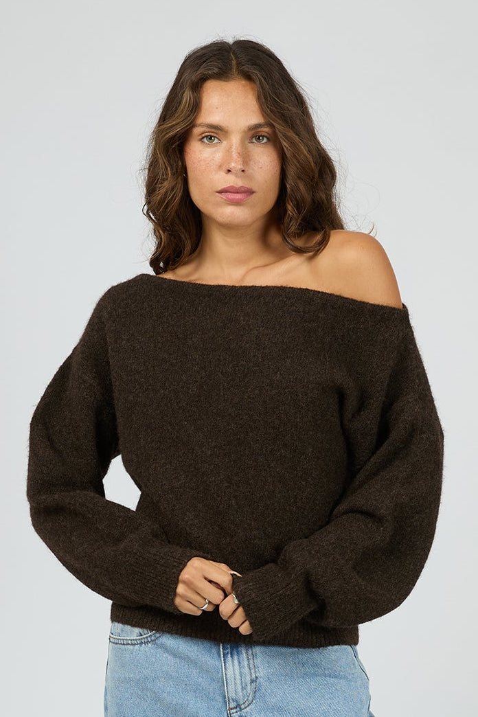 Woman wearing a brown off-shoulder sweater and light blue jeans on a white background