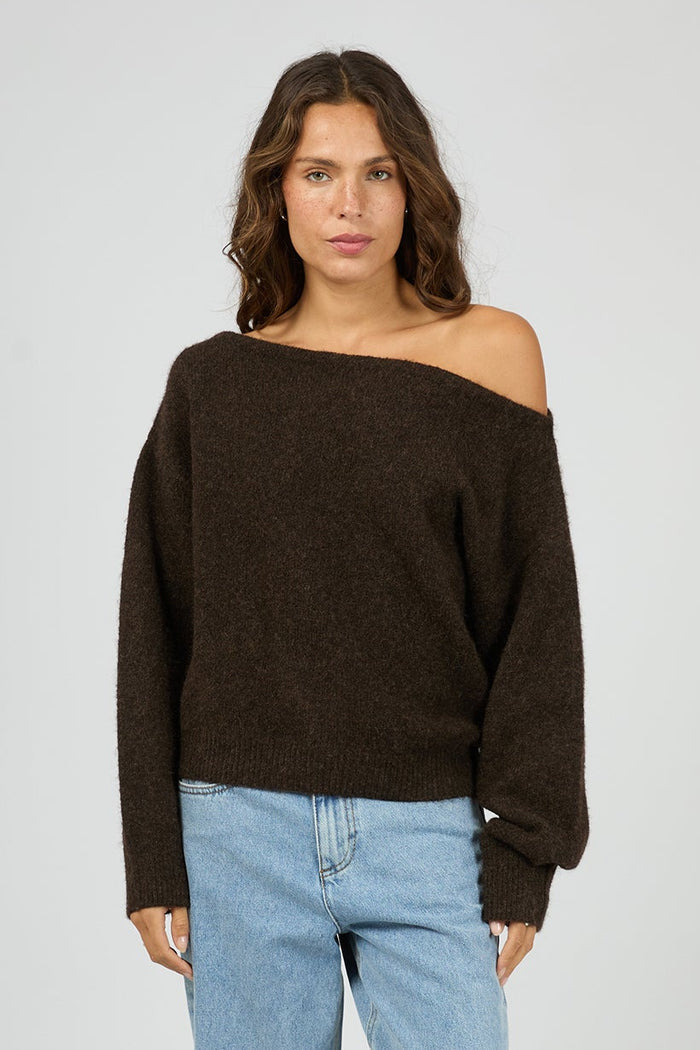 Woman wearing a brown off-shoulder sweater and light blue jeans on a white background