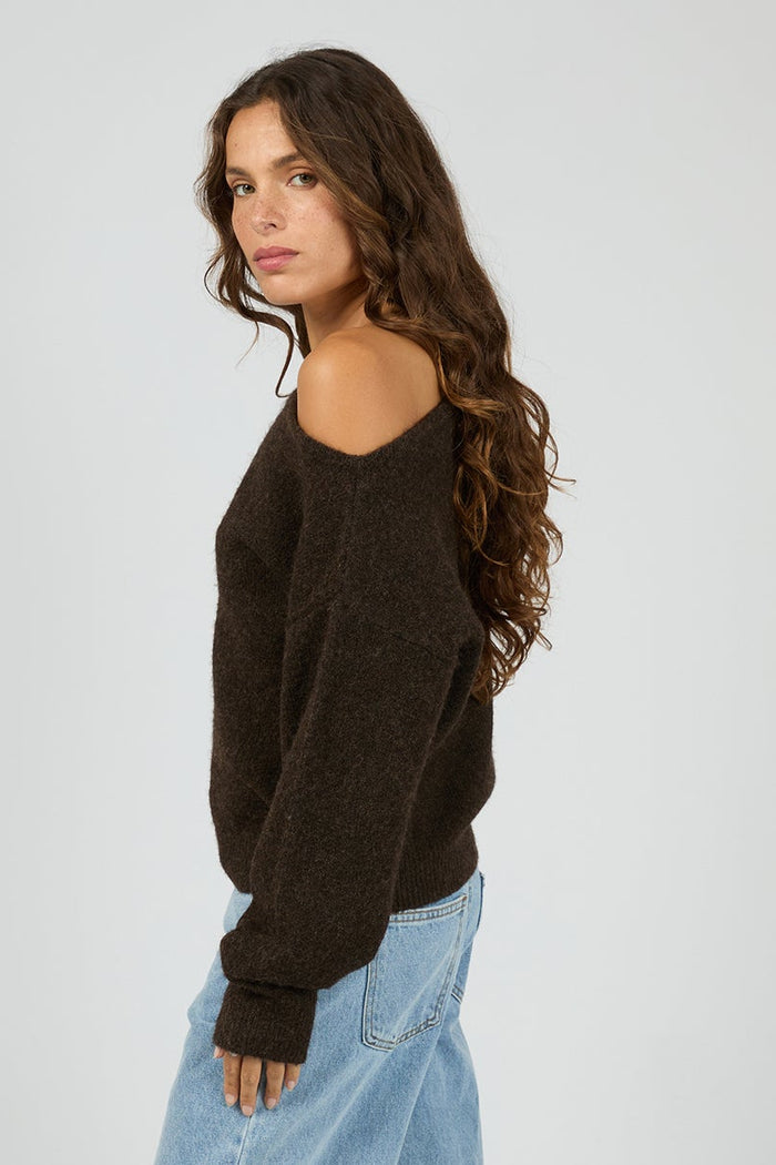 Woman wearing a dark brown sweater and light blue jeans on a white background