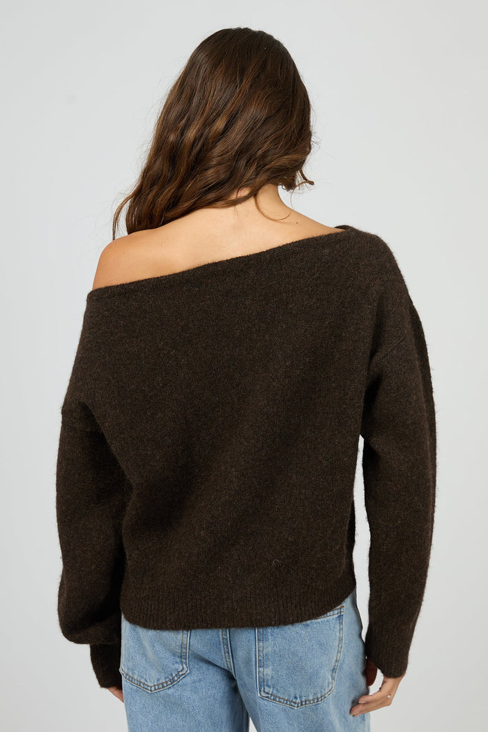 Woman wearing a brown off-shoulder sweater and blue jeans on a plain background