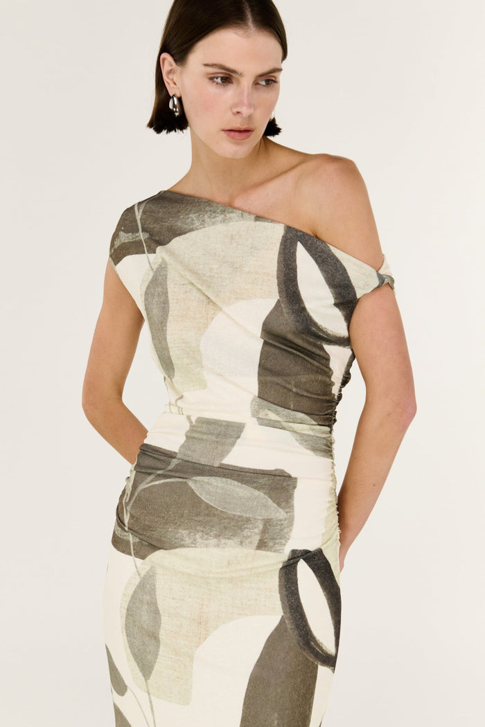 Woman wearing a one-shoulder dress with abstract pattern on a plain background