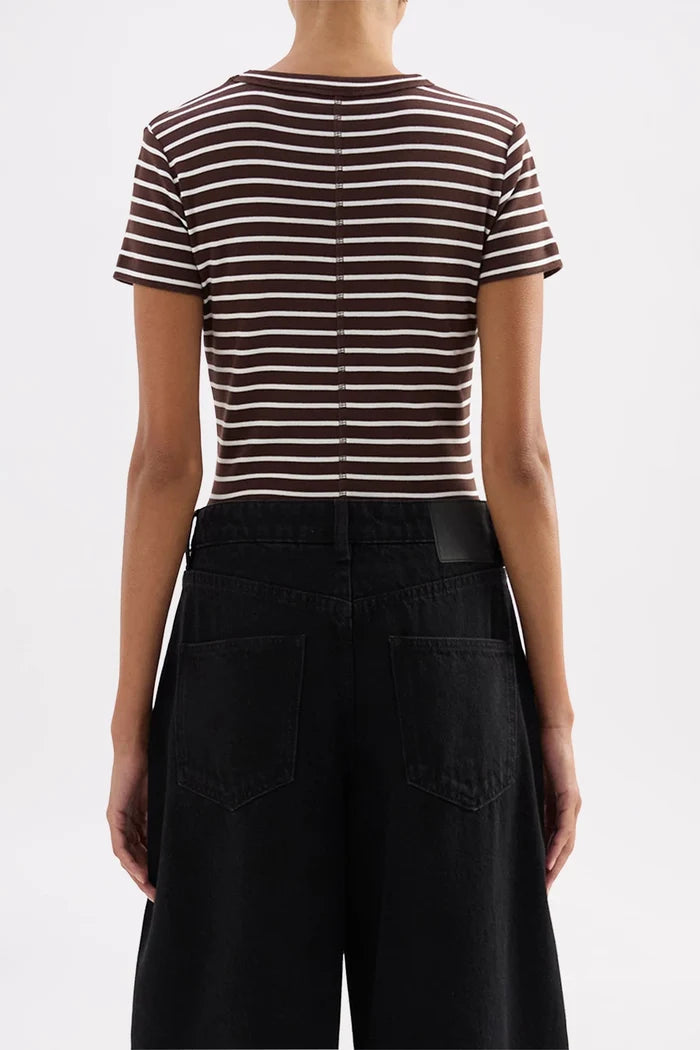 Rear view of a model wearing a brown and white horizontally striped short-sleeve crop top with black wide-leg pants, against a light gray studio background.