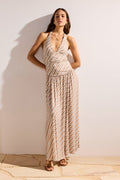 Woman wearing a patterned dress standing against a plain wall.
