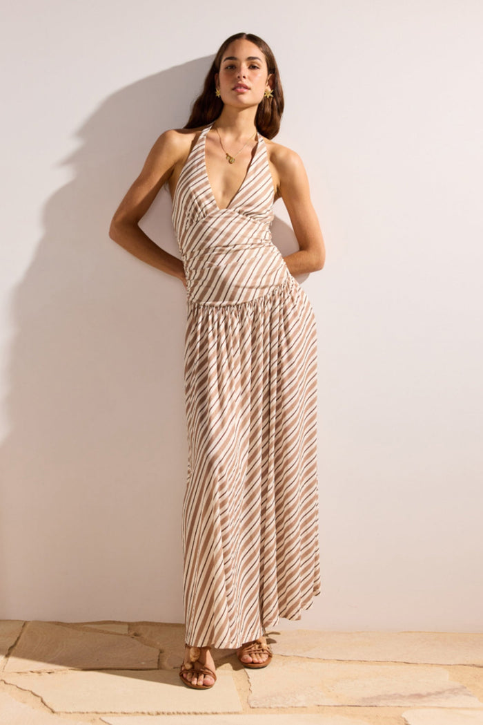 Woman wearing a patterned dress standing against a plain wall.