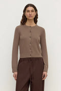 A woman modeling a taupe brown button-up cardigan sweater paired with dark brown drawstring trousers, shot against a plain light gray studio background.