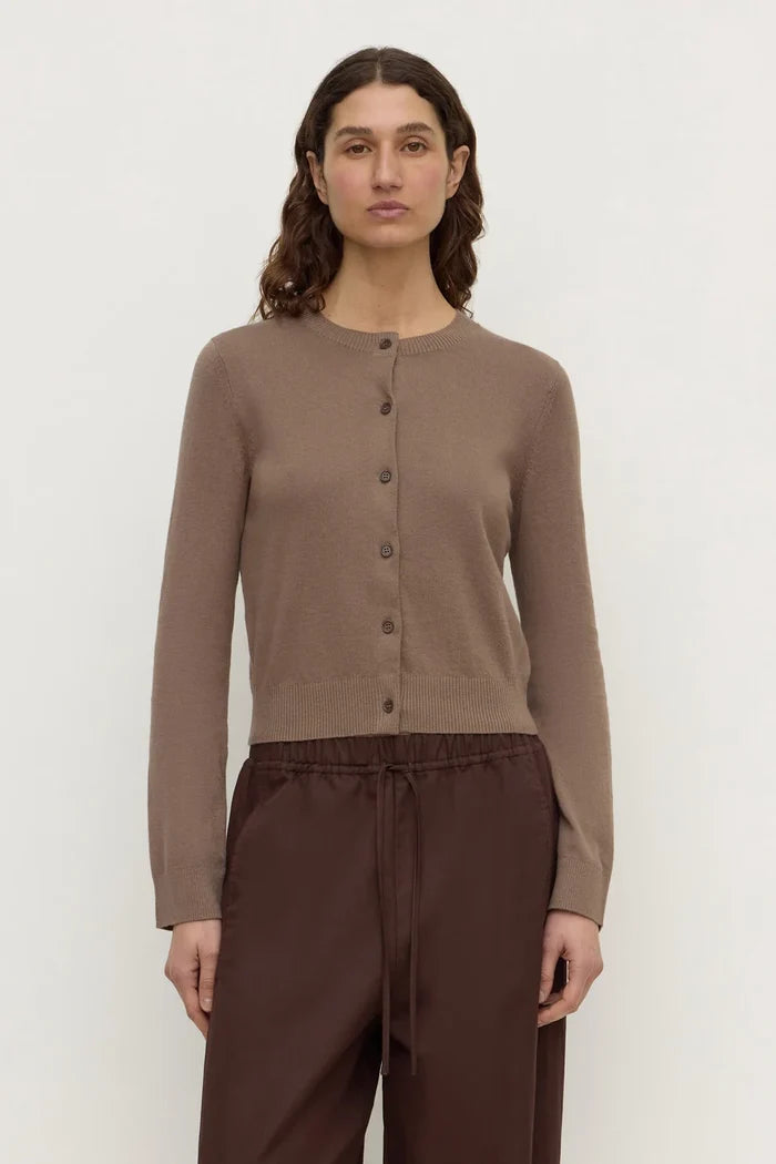 A woman modeling a taupe brown button-up cardigan sweater paired with dark brown drawstring trousers, shot against a plain light gray studio background.