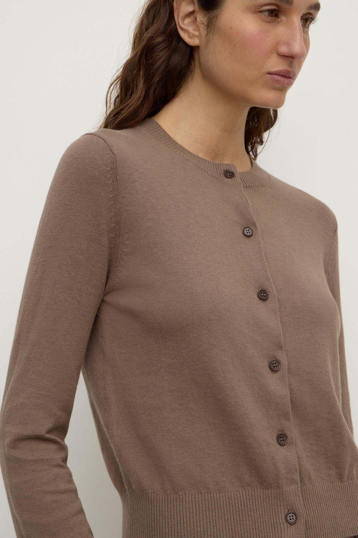 A close-up of a woman wearing a taupe brown long-sleeve button-up cardigan sweater against a plain light background.