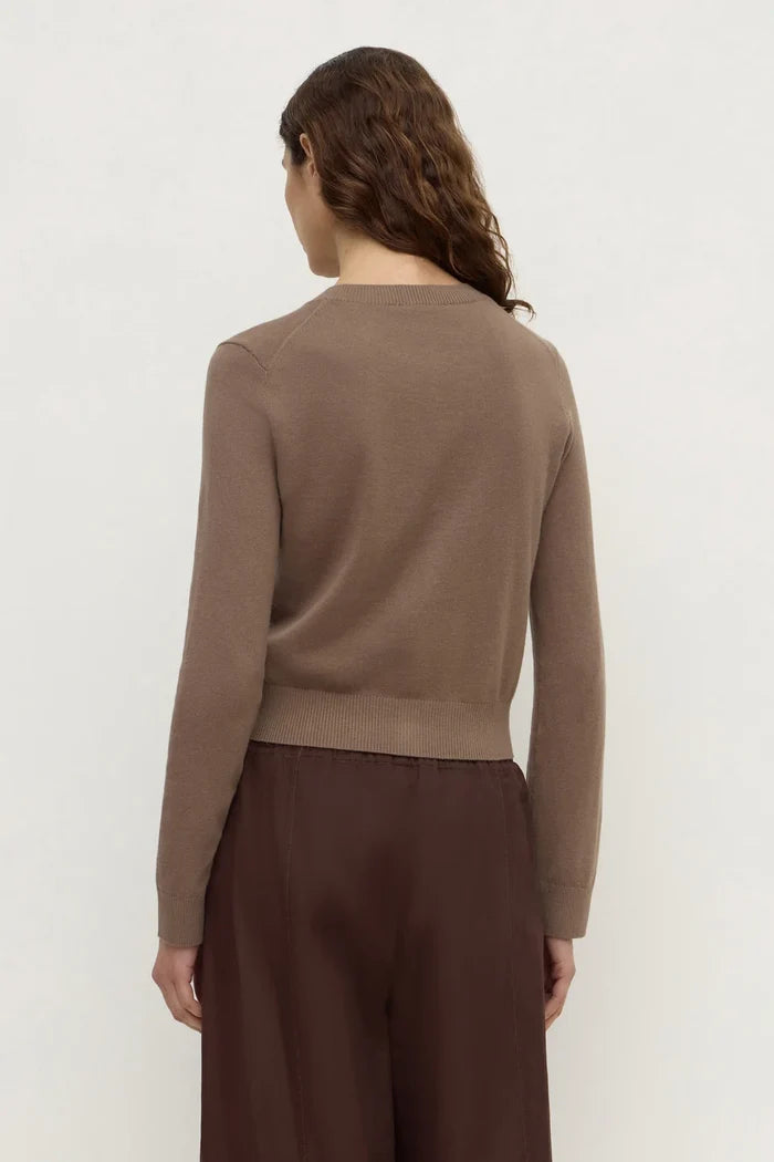 A woman shown from the back wearing a cropped, long-sleeve knit sweater in taupe brown and dark brown wide-leg trousers, set against a plain off-white studio background.