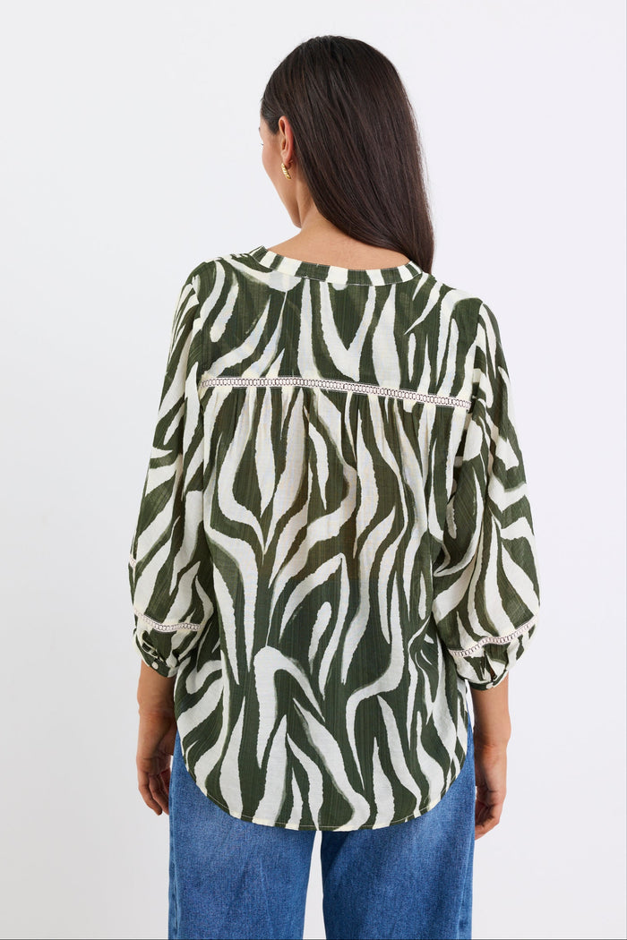 Woman wears a khaki and cream zebra-print shirt with lace inserts and pintuck detail, styled with gold earrings and blue jeans.
col_pattern
