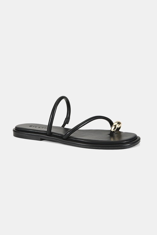 A single black leather flat sandal with a thin strap and a small gold metal ring detail on the toe post, shown against a light gray background.