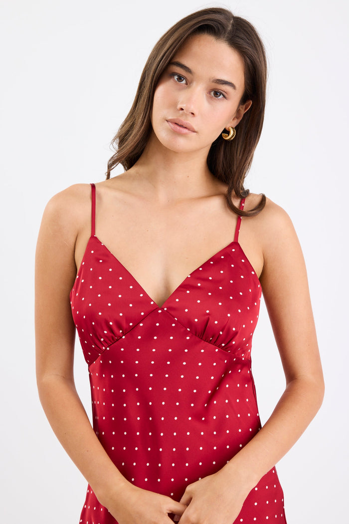 Woman wearing a red satin midi dress with white polka dots, adjustable spaghetti straps, and a bias-cut silhouette, standing against a white background.