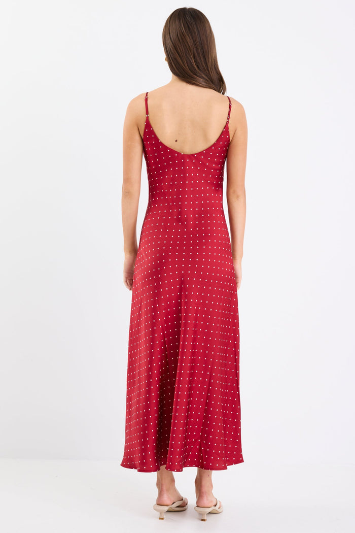 Woman wearing a red satin midi dress with white polka dots, adjustable spaghetti straps, and a bias-cut silhouette, standing against a white background.